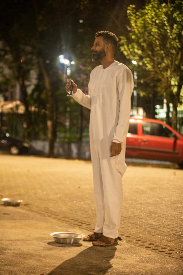 PC, de túnica branca, de pé na praça em frente à Pinacoteca, à noite, ao lado de uma bacia de alumínio