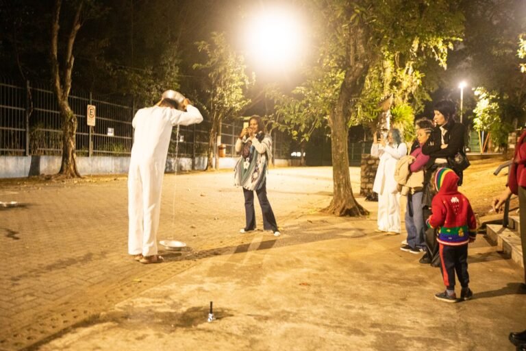 PC derrama água sobre a cabeça diante do público, entre as árvores da praça