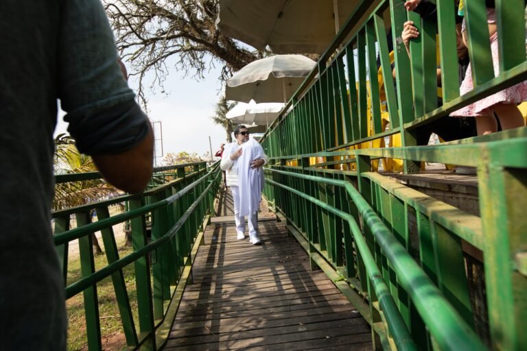 Pio Santana, vestido de branco, caminha pela passarela de gradil verde
