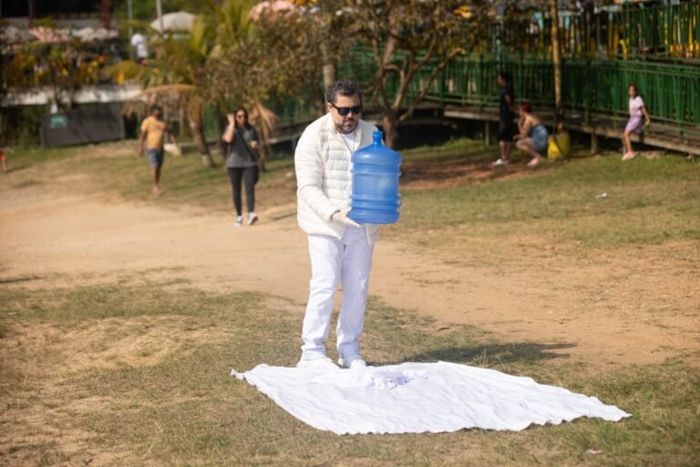 Pio Santana carrega um galão azul sobre um tecido branco estendido no chão de terra