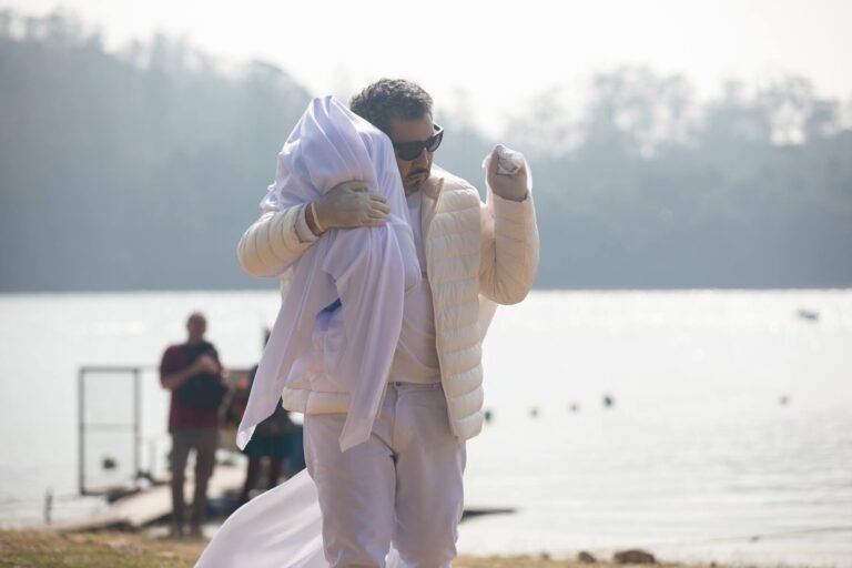 Pio Santana carrega o volume envolto em branco junto ao rosto, com a represa ao fundo