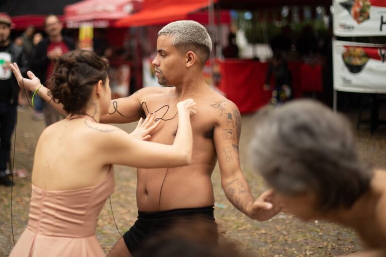 Uma performer passa a linha preta sobre o peito do performer