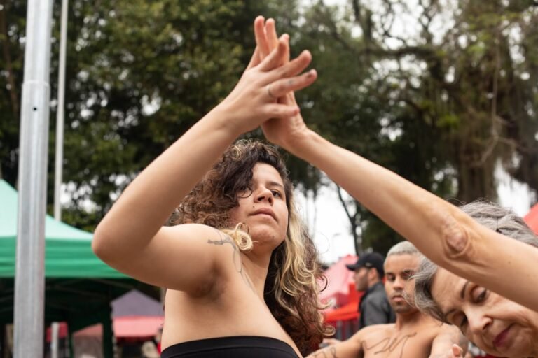 Mãos entrelaçadas no alto entre duas performers