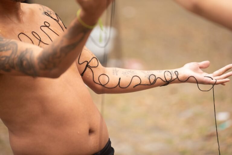 Detalhe do braço e do tronco do performer, com palavras em letra cursiva formadas pela linha preta sobre a pele