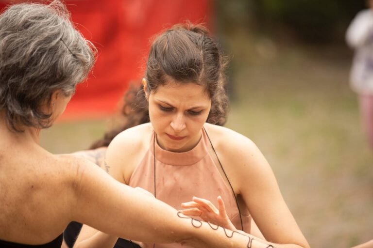 Duas performers frente a frente, uma delas estendendo o braço marcado pela linha preta