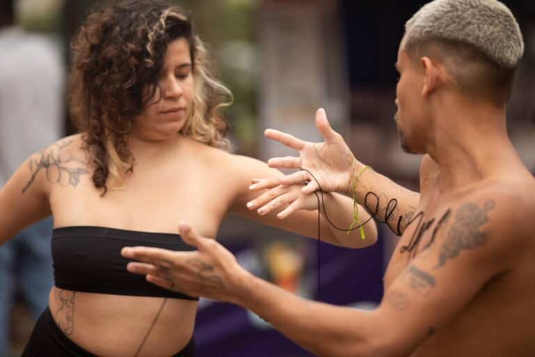 Uma performer e o performer frente a frente, de mãos abertas, com a linha preta passando entre eles