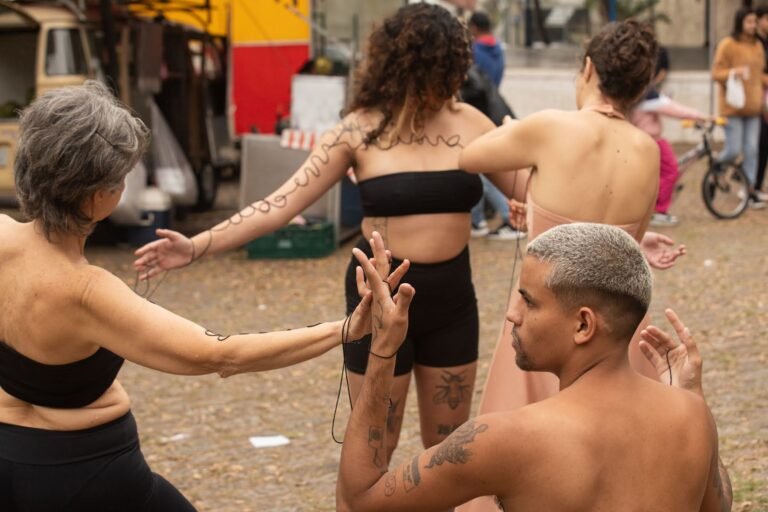 As performers em roda trocam a linha preta, o performer agachado