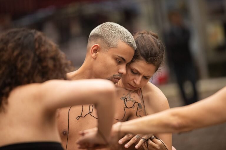 O performer e uma performer abraçados, com palavras de linha preta na pele