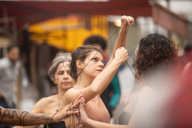 Uma performer ergue a linha preta no alto, cercada pelas outras